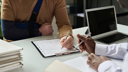 Man with arm in cast signing legal papers on a clipboard